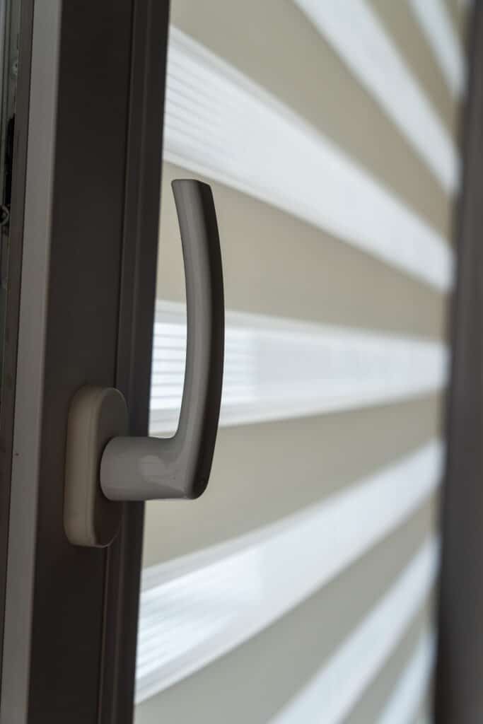 Modern door handle on a window showcasing layered white roller blinds, creating a contemporary interior design aesthetic suitable for home decor. Glass Window Handle